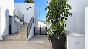 Un espacio exterior limpio y moderno con una escalera que lleva a una puerta, una planta grande en maceta y un cielo azul despejado.