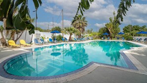 A swimming pool with lounge chairs and umbrellas, surrounded by palm trees and a clear sky.
