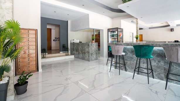 A modern kitchen with a marble countertop, a bar area with stools, and a wooden door.