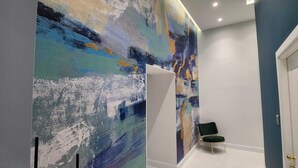 Un pasillo con un cuadro abstracto grande en la pared, una silla negra y una puerta blanca.