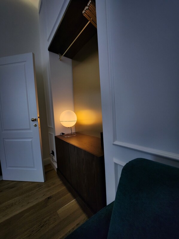 Un couloir avec un plancher en bois, une porte blanche, une console en bois foncé et une lampe.