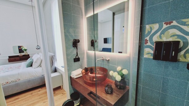 Un baño moderno con ducha envuelta en vidrio, tocador de madera con lavabo de cobre y un espejo grande.
