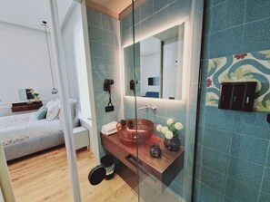 Un baño moderno con ducha envuelta en vidrio, tocador de madera con lavabo de cobre y un espejo grande.