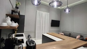 Una cocina moderna con encimera de madera, una cafetera y un hervidor. Hay una zona de estar con sofá y televisor montado en la pared.