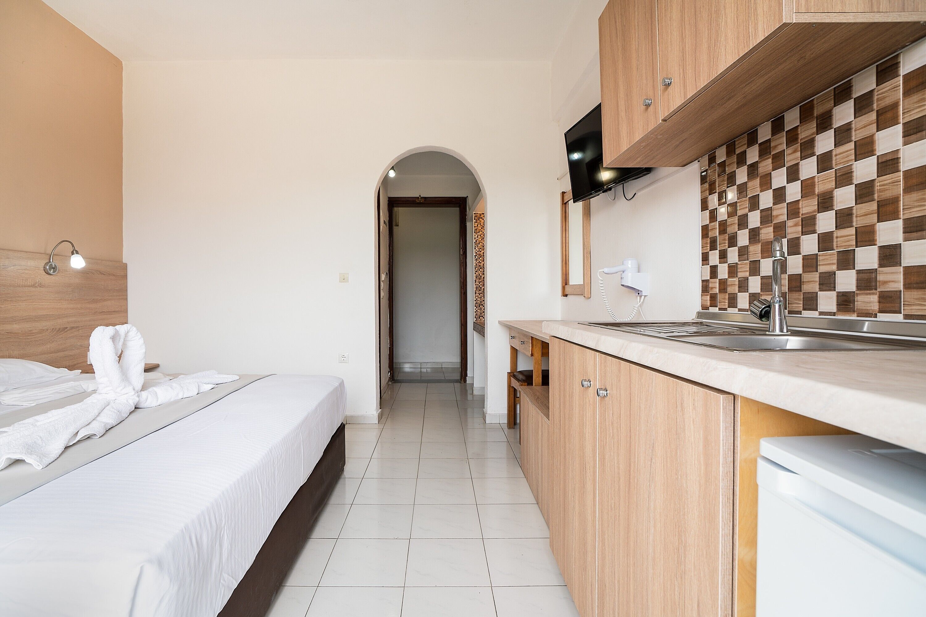Ein Hotelzimmer mit einem Bett, einer Küchenzeile mit Spüle und Schränken sowie einem Fernseher, der über dem Tresen angebracht ist.