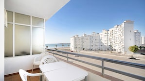 Ein Balkon mit weißem Tisch und Stühlen, der auf einen Strand und eine Reihe weißer Gebäude blickt.