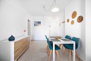 A dining area with a white table, teal chairs, a wooden cabinet, and a hanging light fixture.