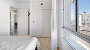 Ein Schlafzimmer mit Bett, Kleiderschrank und einem Fenster mit Blick auf Gebäude.