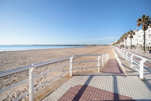 A beach promenade with a tiled walkway, white railings, and palm trees.