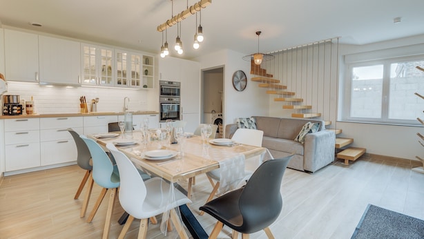 A modern kitchen with white cabinets, a dining table set with chairs, and a staircase leading to a loft area. - Holiday Home 'Le Banc Des Hermelles' with Private Terrace, Private Garden and Wi-Fi (Saint-Benoît-des-Ondes)