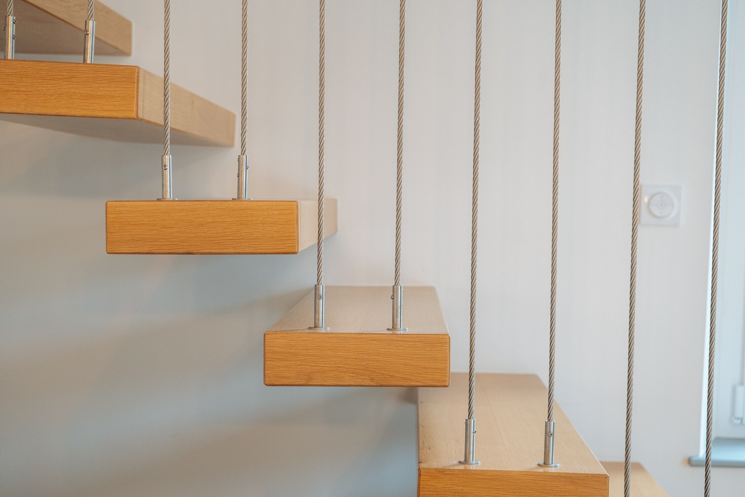 A series of wooden platforms suspended by metal chains against a plain wall.