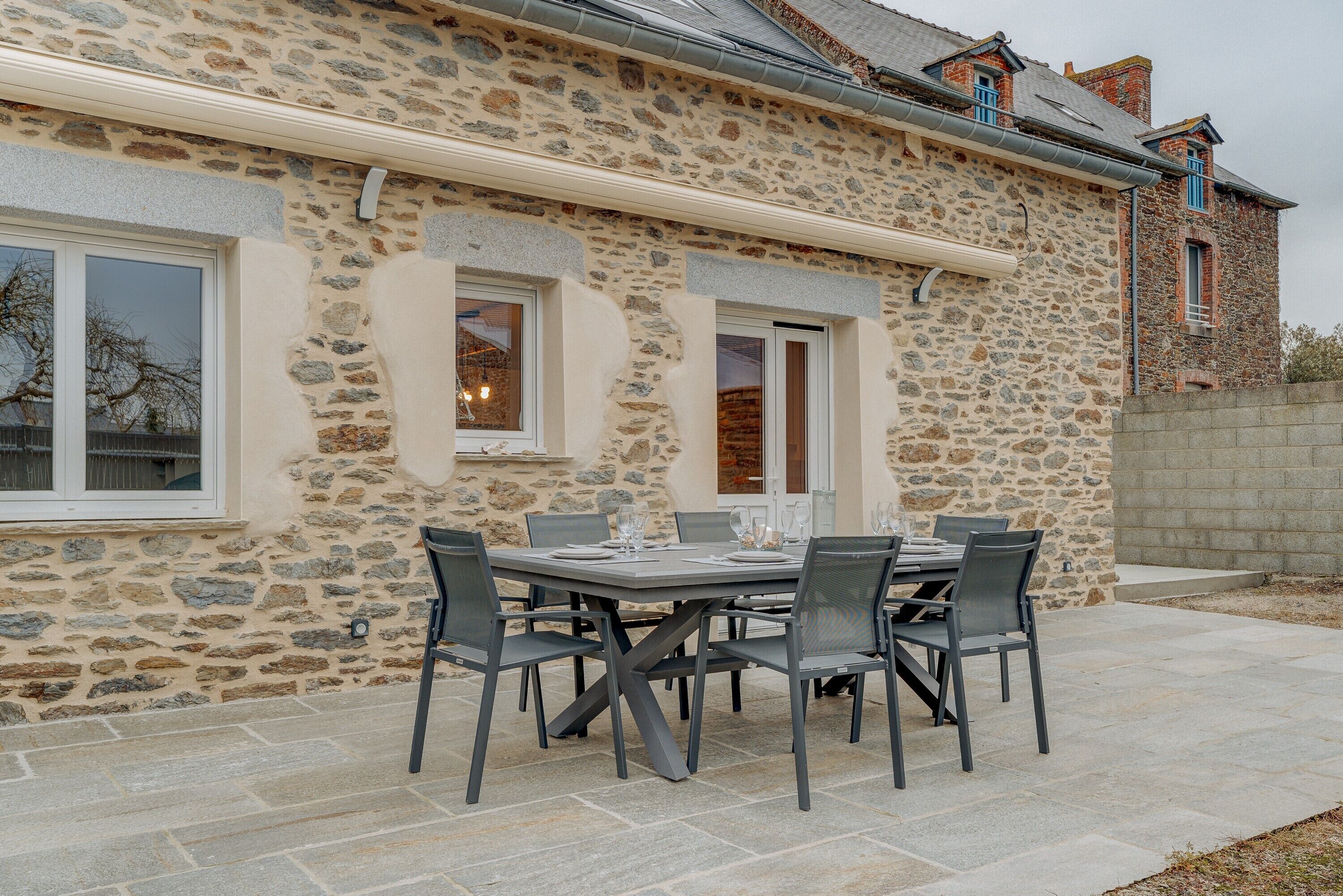A stone building with a patio table and chairs, a window, and a stone wall.