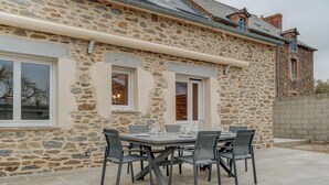 A stone building with a patio table and chairs, a window, and a stone wall. - Holiday Home 'Le Banc Des Hermelles' with Private Terrace, Private Garden and Wi-Fi (Saint-Benoît-des-Ondes)