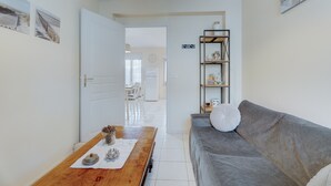 Una habitación con un sofá gris, una mesa de madera con adornos, una puerta blanca y un estante con diversos objetos.