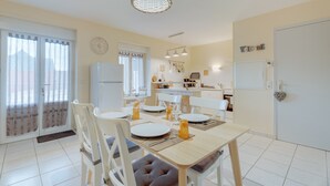 Un comedor con una mesa dispuesta para cuatro, sillas, una lámpara colgante y una cocina al fondo.