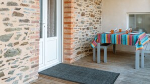 Un muro de piedra, una puerta, una mesa con mantel a rayas y una silla.