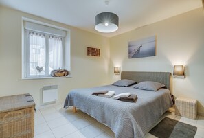 A bedroom with a bed, a window with curtains, a wall-mounted shelf, a painting, and a bedside lamp.