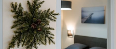 A wall-mounted pine branch decoration with pine cones, a bed with grey bedding, and a painting on the wall.