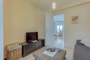 Un salon avec une télévision, un panier en osier, un canapé et, au fond, un coin repas.