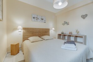 Une chambre à coucher bien aménagée, avec un grand lit, des lampes de chevet, un petit tabouret en bois, une table de chevet avec une lampe et des œuvres d’art accrochées au mur.