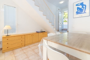 A modern kitchen with wooden cabinets, a dining table, and a staircase leading to another room.