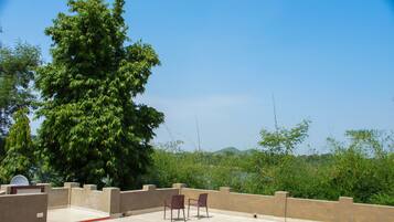A rooftop terrace with two chairs, a tiled floor, and a view of greenery and hills.