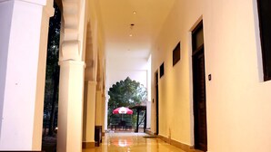 A long, narrow hallway with white walls and a tiled floor. There are columns on the left side, and a door on the right.
