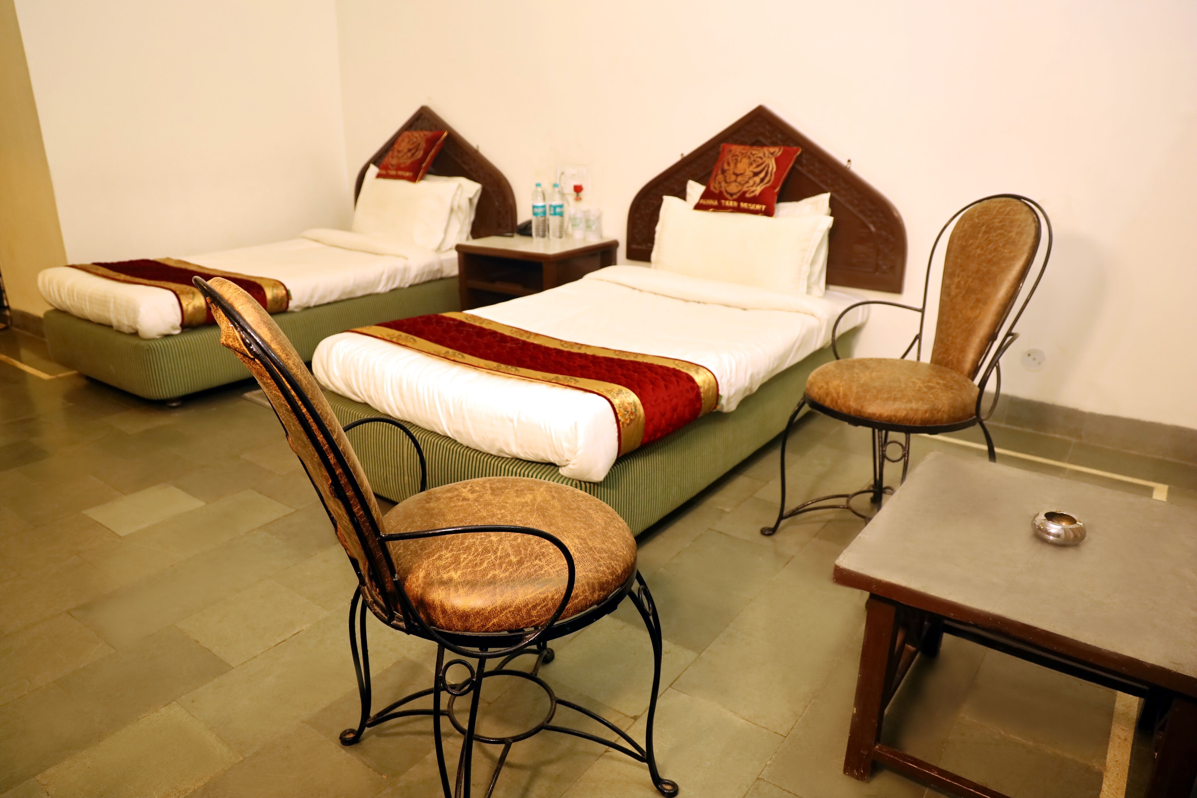 A hotel room with two single beds, a wooden chair, a small table, and a nightstand with a lamp.