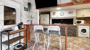 A compact kitchen with a marble backsplash, a flat-screen TV, a bar area with stools, a washing machine, and a clock. - Holiday Home "Casa Tenerife Primera Linea" with Sea Views, 3 Private Terraces and Wi-Fi (tenerife)
