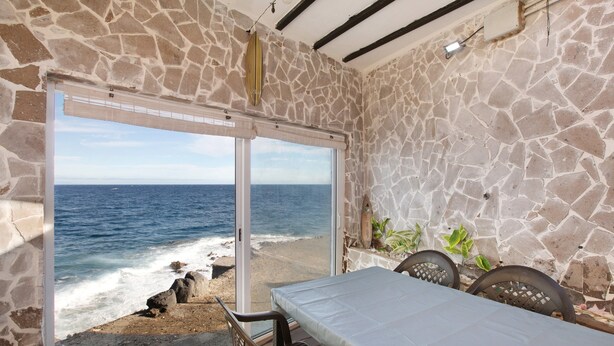 A room with a stone wall, a bed, a table, and a view of the ocean. - Holiday Home "Casa Tenerife Primera Linea" with Sea Views, 3 Private Terraces and Wi-Fi (tenerife)