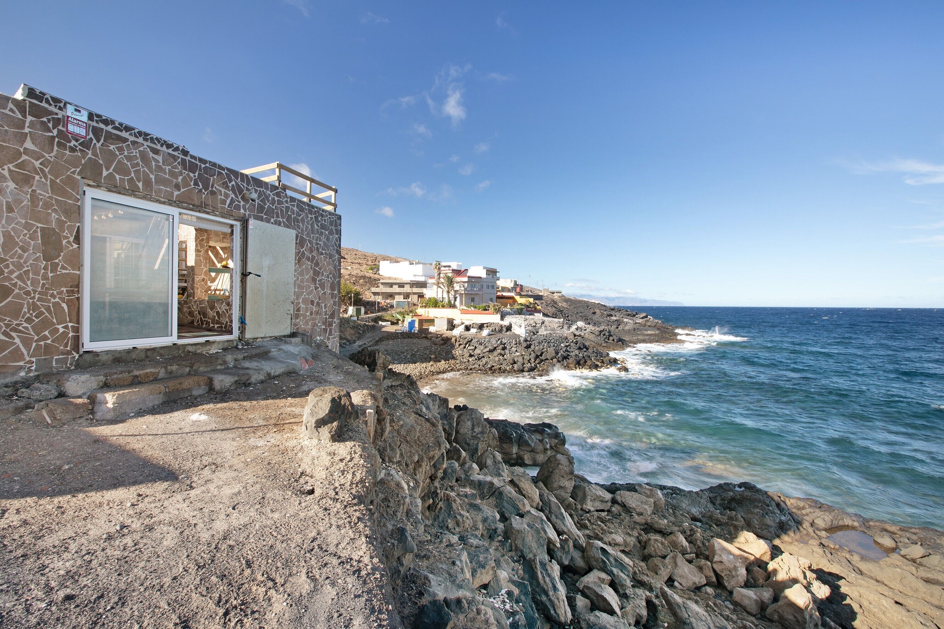 Un edificio costero con fachada de piedra, puerta de cristal y escalones que bajan hacia una costa rocosa.