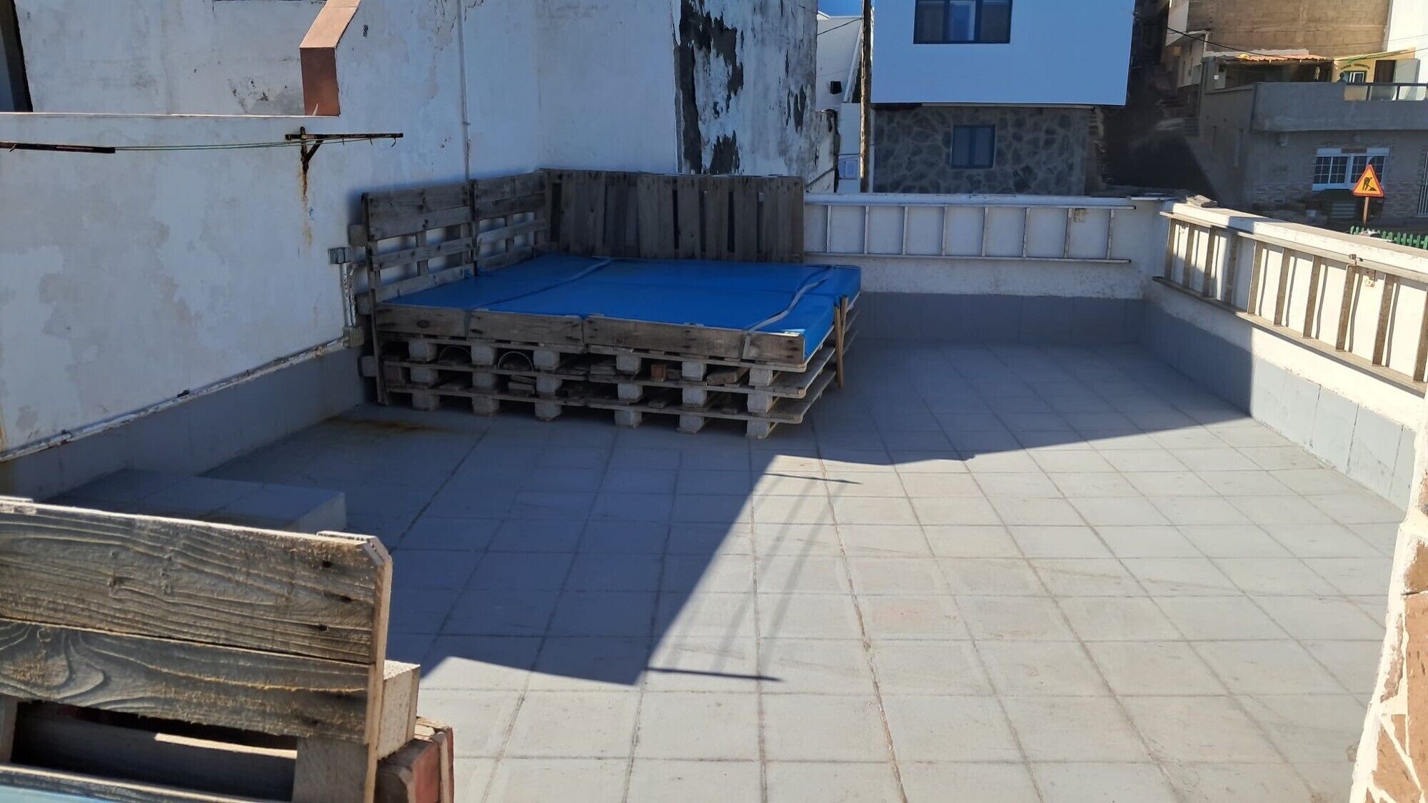 A rooftop terrace with a blue tarp-covered area, surrounded by walls and a railing.