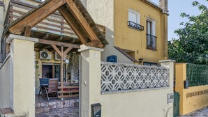 A yellow building with a wooden pergola, a gate, and a patio area with chairs and a table. - Vacation Home "Casa Empuriabrava Con Terraza" with 2 Private Terraces & Private Garden (Castelló d'Empúries)