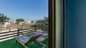A balcony with two wooden lounge chairs and a small table, a wooden fence, and a view of buildings in the distance. - Vacation Home "Casa Empuriabrava Con Terraza" with 2 Private Terraces & Private Garden (Castelló d'Empúries)