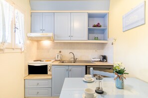 Una cocina compacta con microondas, tostadora, lavamanos y una pequeña mesa de comedor con un florero.