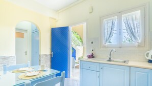 Una cocina con una puerta azul, una mesa de comedor con platos y una ventana con cortinas.