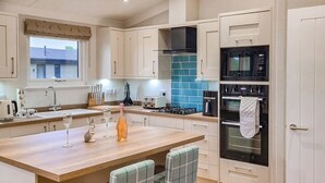 A modern kitchen with a central island, a built-in oven, and a window overlooking a house. - Rabbit Lodge is designed to provide you with a luxurious and comfortable stay. (Thorney, Nr Lincoln)