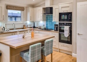 A modern kitchen with a central island, a built-in oven, and a window overlooking a house. - Rabbit Lodge is designed to provide you with a luxurious and comfortable stay. (Thorney, Nr Lincoln)