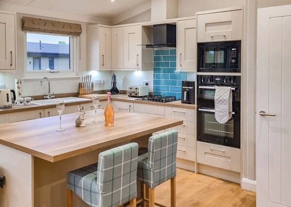 A modern kitchen with a central island, a built-in oven, and a window overlooking a house.