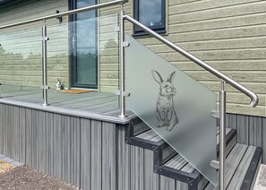 A modern exterior with a glass door, metal railing, and a wooden deck. - Rabbit Lodge is designed to provide you with a luxurious and comfortable stay. (Thorney, Nr Lincoln)