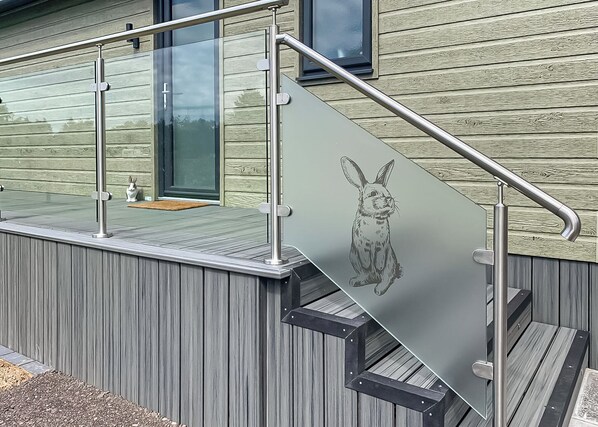 A modern exterior with a glass door, metal railing, and a wooden deck.