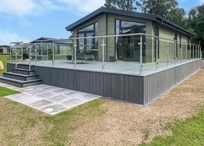 A modern building with a glass balcony, a wooden deck, and a metal railing. - Rabbit Lodge is designed to provide you with a luxurious and comfortable stay. (Thorney, Nr Lincoln)
