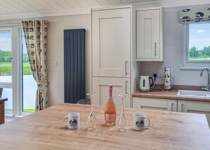 A kitchen with a wooden table, a bottle of wine, and two mugs. - Rabbit Lodge is designed to provide you with a luxurious and comfortable stay. (Thorney, Nr Lincoln)