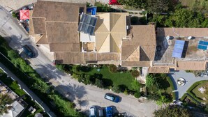 Vista aérea de un edificio con varias secciones en el techo, paneles solares y un estacionamiento con varios coches.