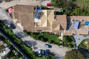 Vista aérea de um edifício com várias seções de telhado, painéis solares e uma área de estacionamento com vários carros.