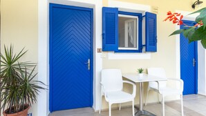 Una habitación con una puerta azul, una mesa blanca y dos sillas, y una planta en maceta.