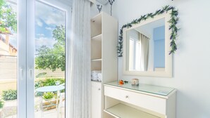 Una habitación con puerta de cristal corredera que da a un patio, un tocador blanco con espejo y una pequeña mesa con una silla afuera.