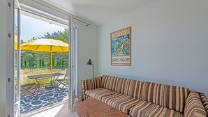 Una habitación con un sofá a rayas, una mesita pequeña y un paraguas amarillo en el exterior.