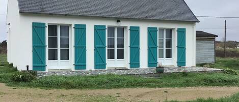 A white building with teal shutters, a grey roof, and a stone foundation.