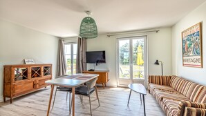 Amplia sala de estar con una mesa de comedor de madera, un sofá a rayas, un televisor y un gran ventanal con vistas a la vegetación.